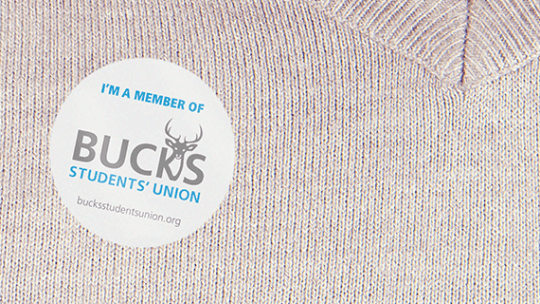 A close-up of a beige jumper with a Bucks Students' Union rounded sticker on.