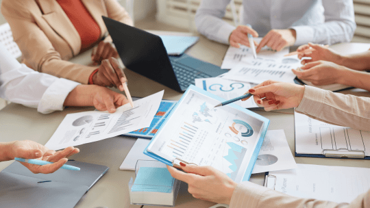 Data presented in bar charts and graphs on paper being held by people in a business meeting