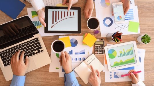 Data presented on bits of paper on a table with 3 people assessing the data in a business meeting