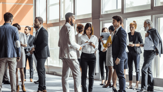 People dressed up smartly in suits talking to one another in small groups whilst standing up