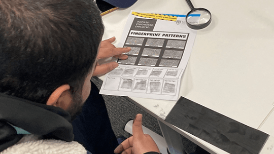 A Criminology student sat at a desk putting his finger print onto a piece of paper