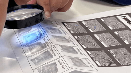 A magnifying glass with a light looking at a finger print left on a bit of paper