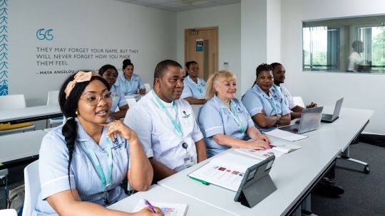 Eight nursing students sat in their uniform in a classroom facing the front of the room with textbooks open