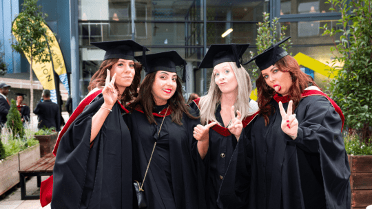 Four graduates stood next to each other posing in front of the camera