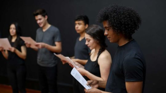 Five students stood in a line reading their scripts in a music class