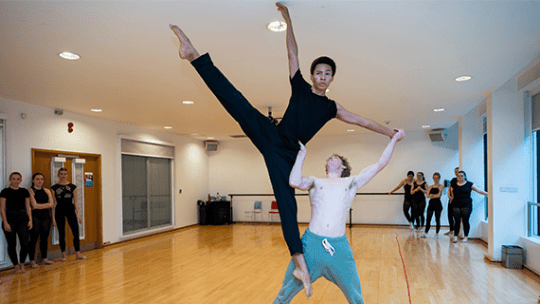 A dance student holding a fellow dance student up in the air as they perform a routine