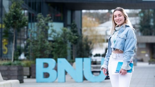 Female student outside BNU sign at High Wycombe campus