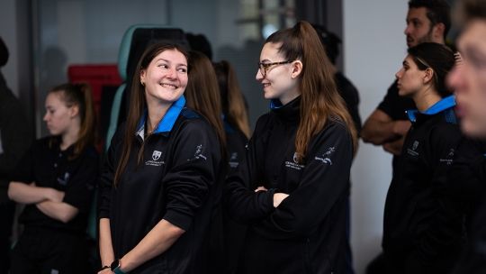 Two Sports Therapy students in uniform looking and smiling at one another