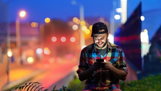 A student in front of a bright background looks down at their phone.