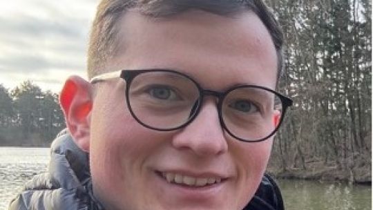 A headshot of BNU George Kingston-rayes wearing glasses stood in front of a lake.
