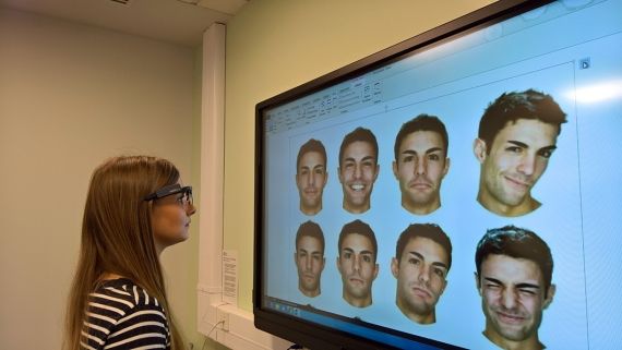 A lady looking at a computer screen which has 9 male faces on