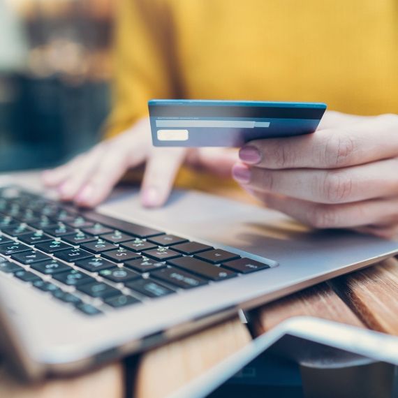 Someone holding a credit card in their left hand with their right hand on a laptop