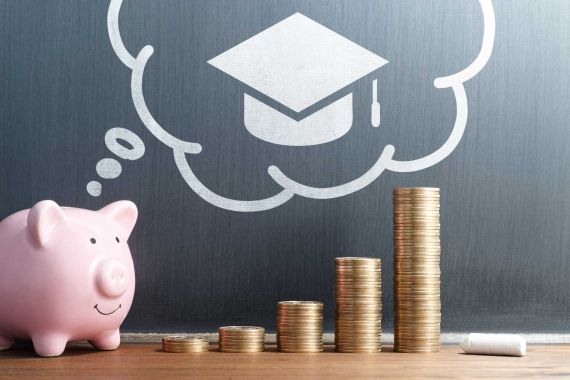 Piggy bank and money on table with graduation hat in background