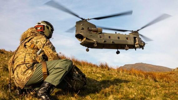 Military person in camouflage and a Chinook taking off