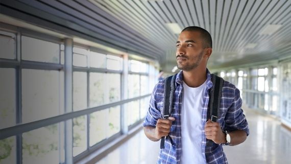 student with backpack standing in well-lit corridor