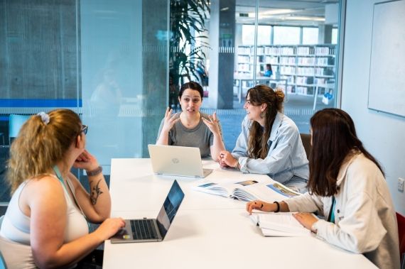 Lecturer and students talking at a table in one of the study rooms in the Library