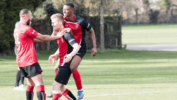 Three BNU footabllers celebrate scoring a goal. One players gives another a piggy back and then goes to hug the third person