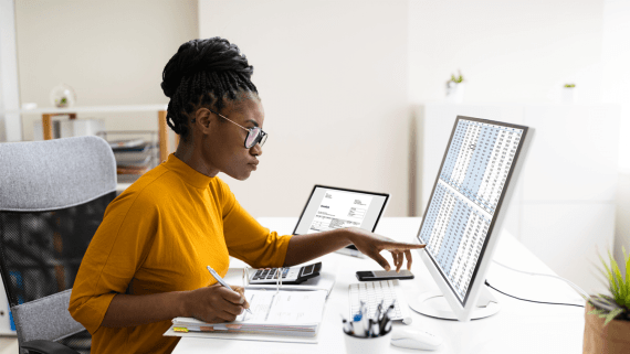 A woman sat at a desk pointing at her computer screen