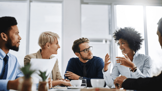 Five members of staff sat around a table talking to one another looking at one another