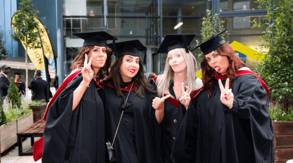 Four graduates stood next to each other posing in front of the camera