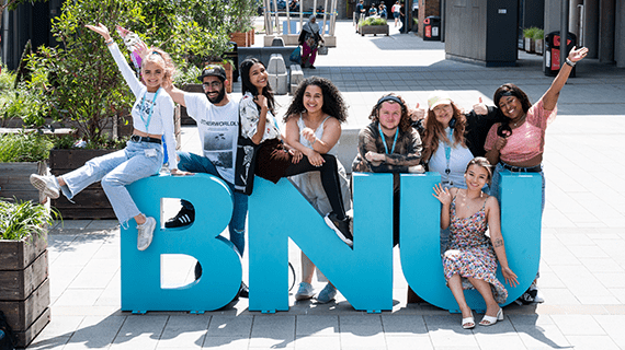 BNU students stood and sat around the BNU letters on the concourse, with their hands up in the air smiling towards the camera