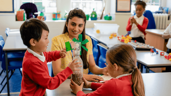 Two primary school children playing with toys as their teacher watches on.