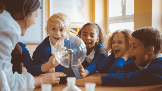 Four primary school children sat around a table smiling toward their teacher.