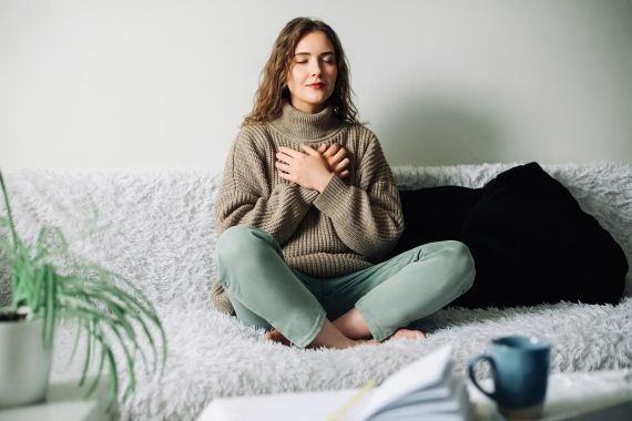 A person sitting on the couch and meditating with their palms on their chest