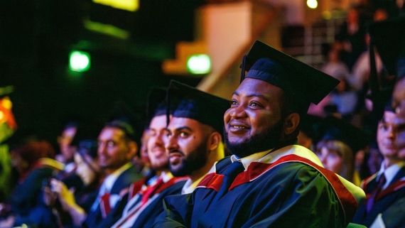 Students sat down smiling in a theatre as they watch fellow students graduate.