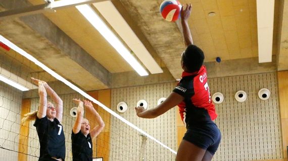 two girls defending a volleyball shot over the other side of the net