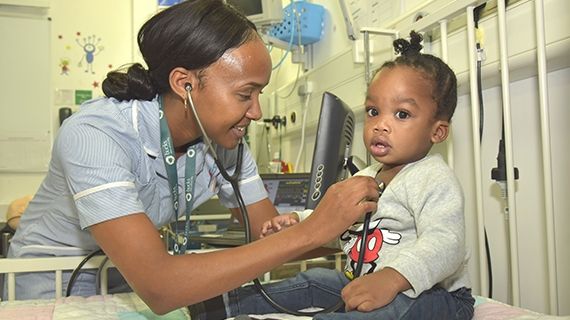 Nurse attends to a child who is sat up in bed