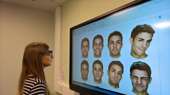 A lady looking at a computer screen which has 9 male faces on