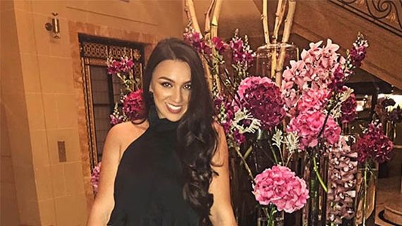 Nadina leaning on a table with large pink and purple flowers behind her