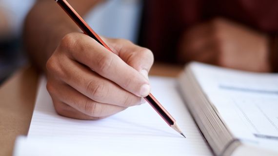 A student with a pencil in their right hand about to write on a bit of paper