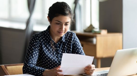 Student reading a piece of paper at a desk next to a laptop