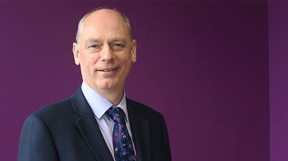 Nick Braisby head and shoulders picture stood in front of a purple coloured wall