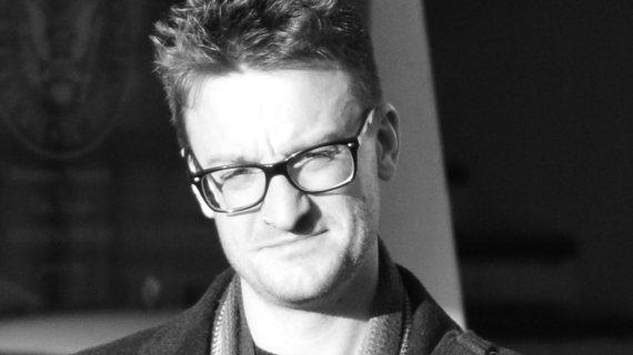 Head and shoulders photo of a smiling Paul Fields wearing glasses with a coat and scarf on