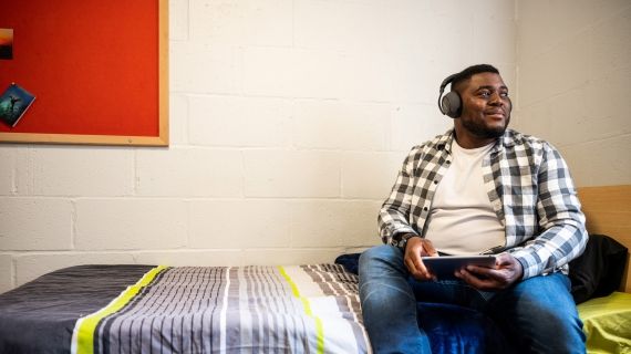 Male student sat on bed and listening to music