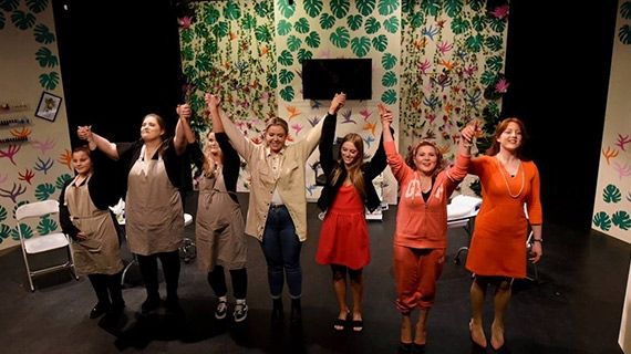 7 performing arts students holding one another's hands in the air on stage following a performance