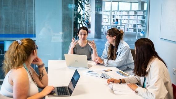 Lecturer and students talking at a table in one of the study rooms in the Library