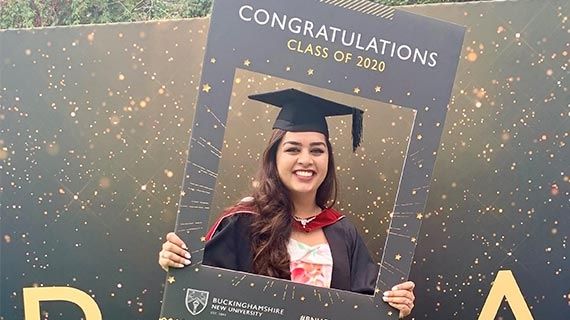 Fareeha Ahmed in graduation cap and gown, holding a picture frame with the words 'Congratulations class of 2020'