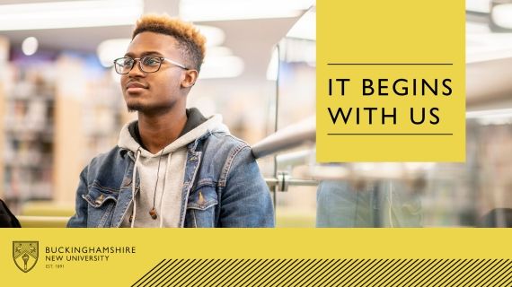 A student wearing glasses stood in a library smiling with 'it begins with us' text over a yellow box on top of the image