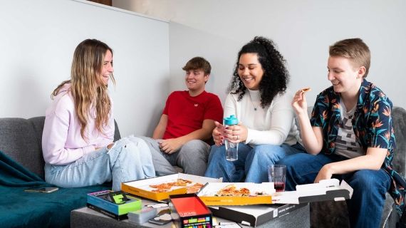 Four students eating pizza in a lounge area in Windsor House accommodation