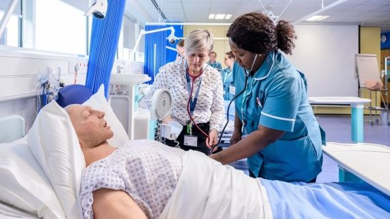 A BNU student nurse alongside a hospital bed which has a male dummy in
