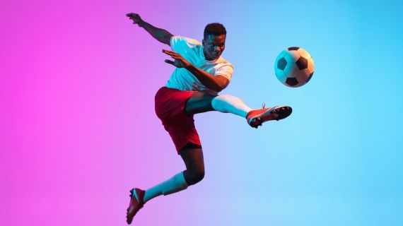 young man kicking a football against coloured backdrop