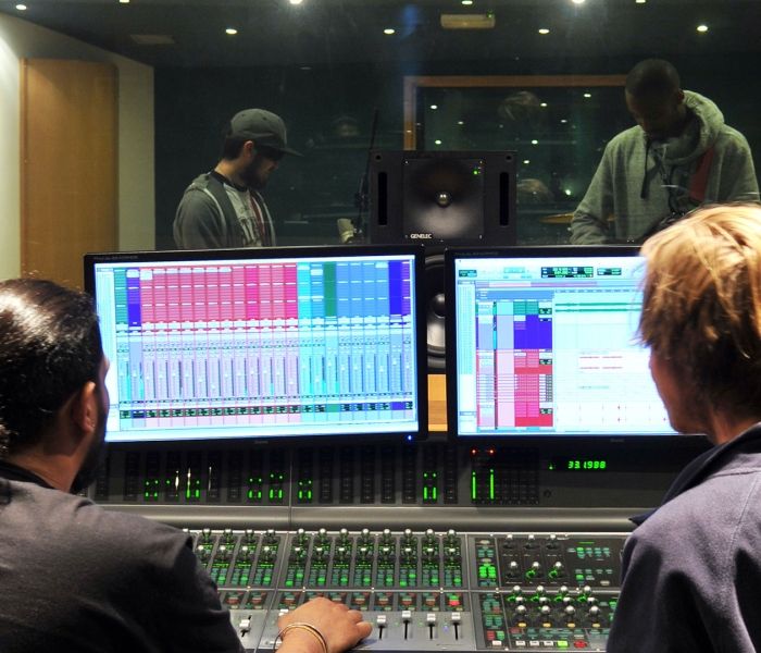 two men looking at two screens in a music studio 