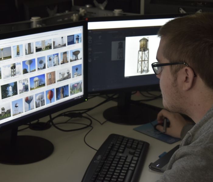 Student with glasses looking at two computer screens