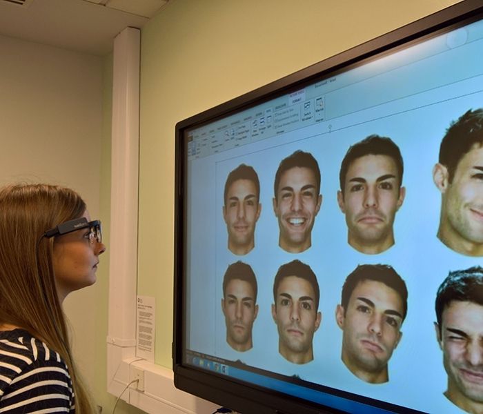A lady looking at a computer screen which has 9 male faces on