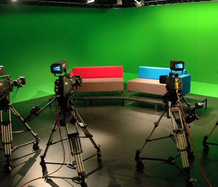 Four cameras pointing towards a sofa with a green screen behind it