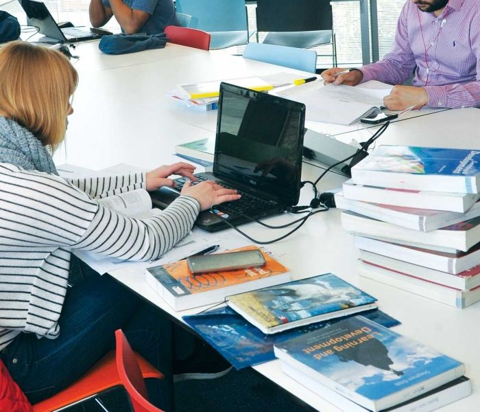 BNU female student in library with lots pf books round her and laptop